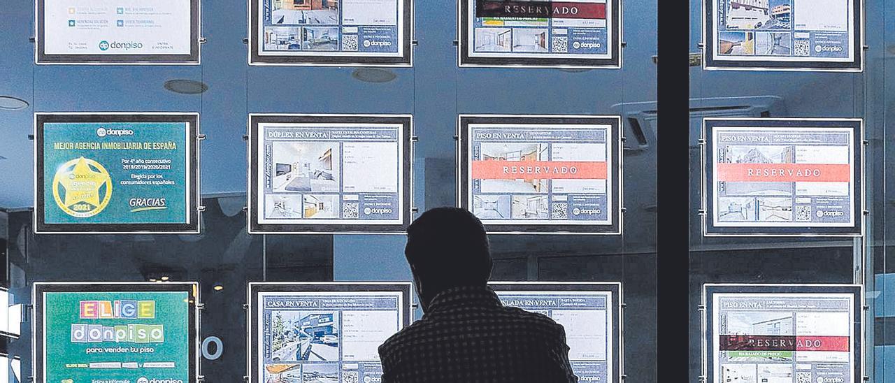 Un hombre mira las ofertas de vivienda en el escaparate de una inmobiliaria.