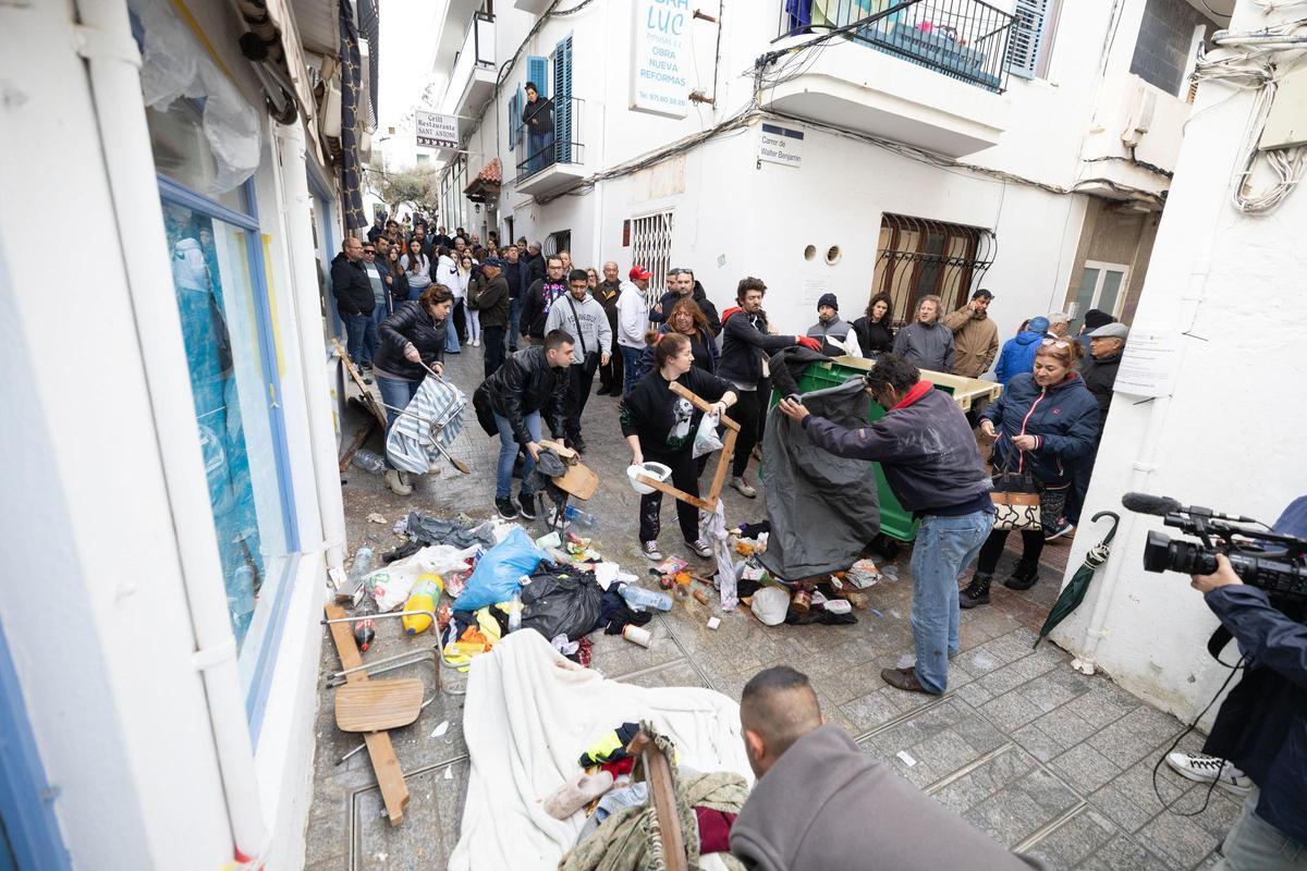 Algunas personas limpian la calle y lanzan los enseres de los okupas a un contenedor de basura.