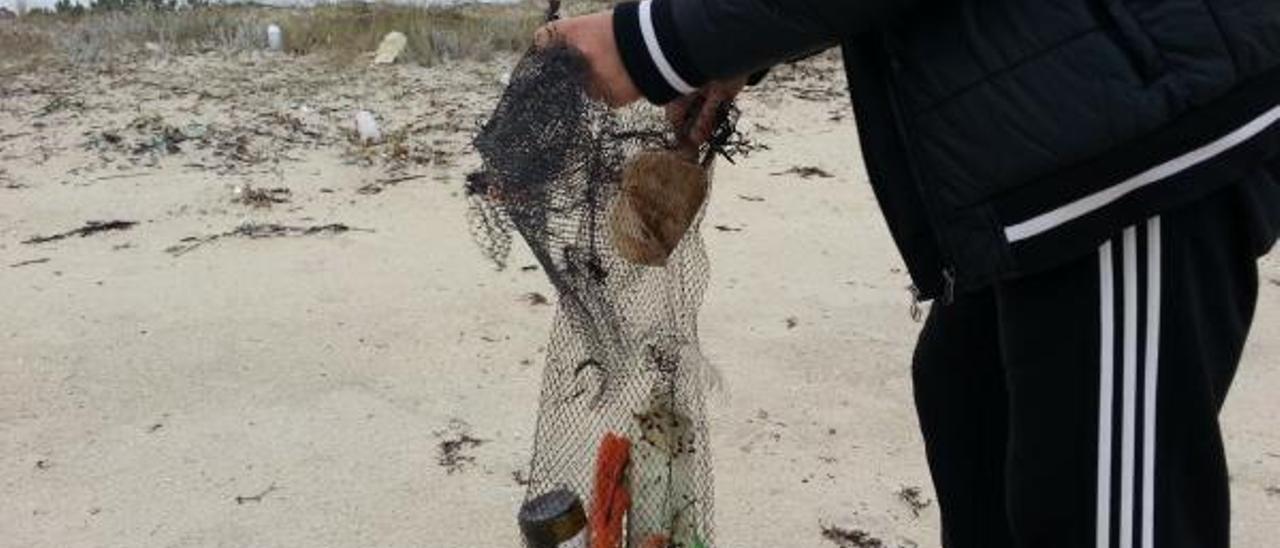 Un vecino recoge residuos en la playa grovense de Raeiros