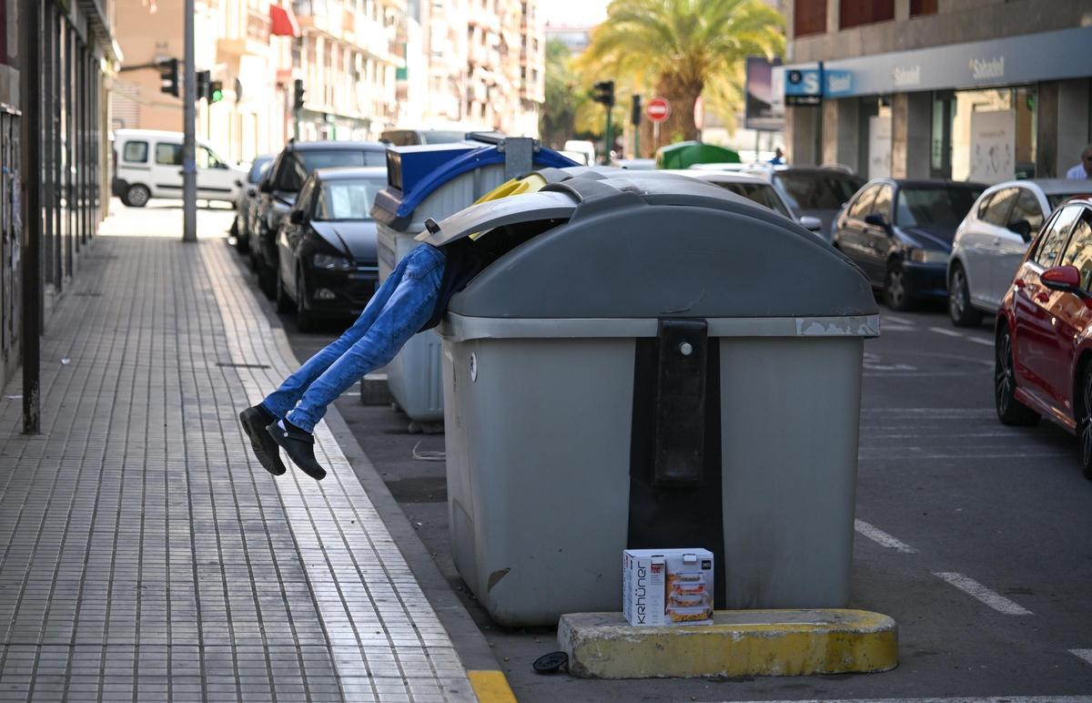 Una persona busca comida o algo que poder revender en un contenedor en Elche