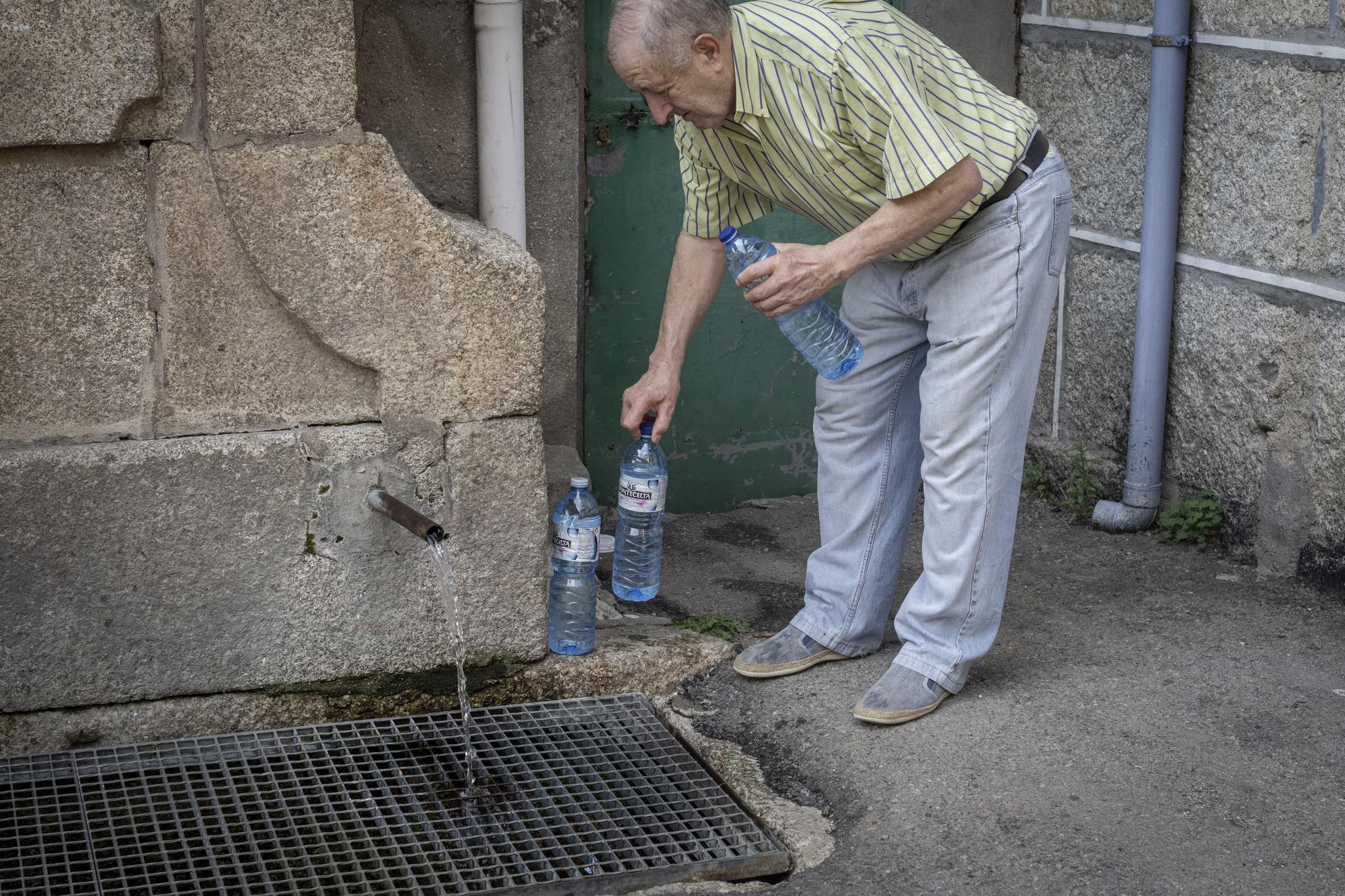 Un hombre rellena varias botellas en Francelos con agua de la fuente.