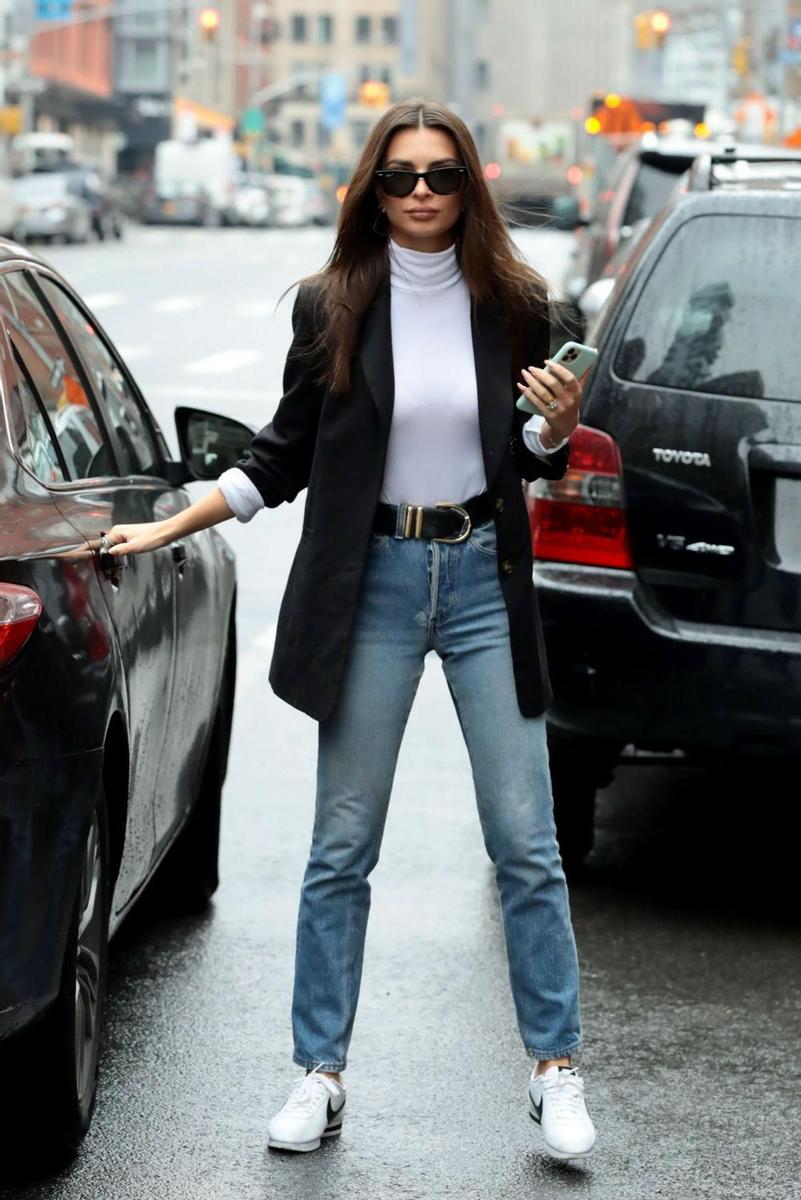 Emily Ratajkowski con un look de casual friday combinando jeans y deportivas blancas con una americana negra