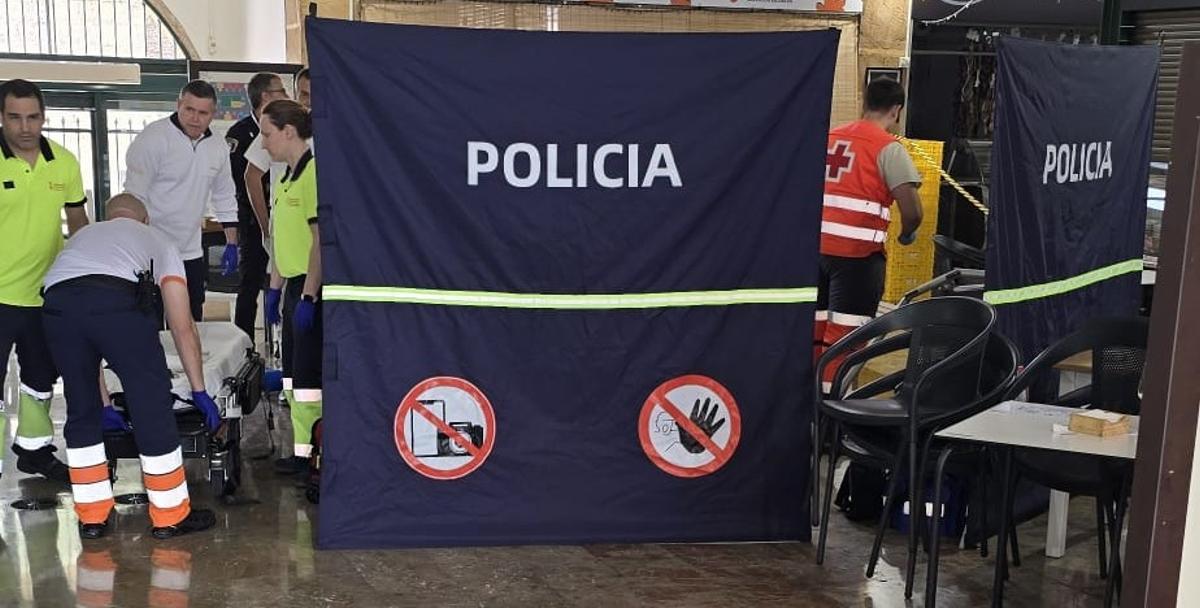 Los facultativos y sanitarios atienden al cliente que ha sufrido el infarto tras la mampara colocada por la Policía Local