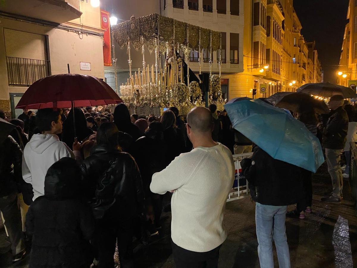 Vecinos obserrvan los pasos con paraguas durante la tarde de este Domingo de Ramos en Elche