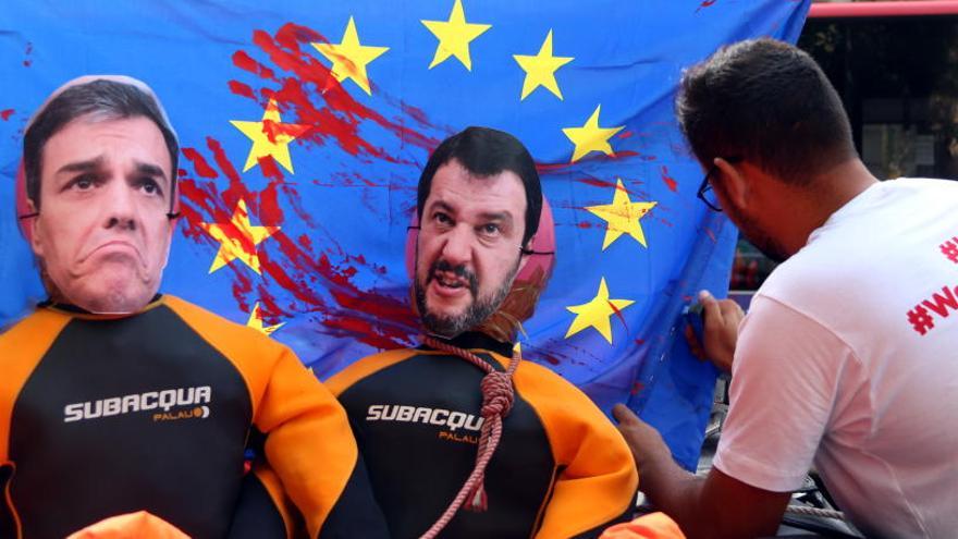 Un dels manifestants col·locant la bandera de la UE tacada de sang darrere de dos ninots que representen Sánchez i Salvini