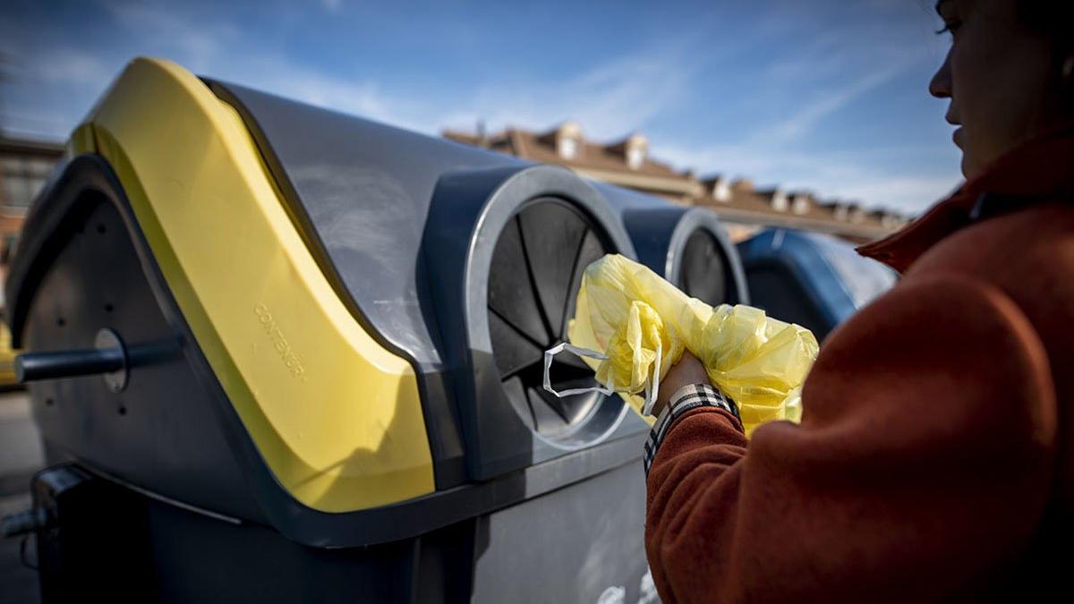 Una mujer deposita un envase de plástico en el contenedor amarillo