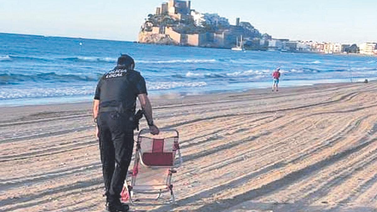 Un policía local de Peñíscola retira una silla sin propietario en la playa Norte del municipio costero más turístico de la provincia. Esta práctica está considerada una infracción leve, con multas de hasta 750 euros.