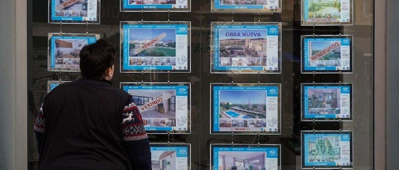 Una mujer mira la oferta de viviendas en el escaparate de una inmobiliaria.