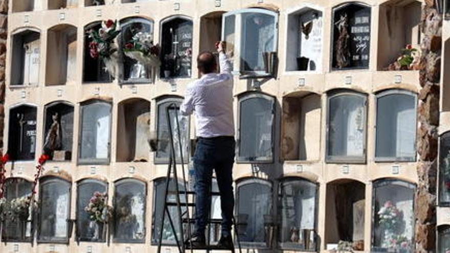 Una home sobre una escala arreglant amb flors una tomba al cementiri de Montjuïc, l&#039;1 de novembre del 2020