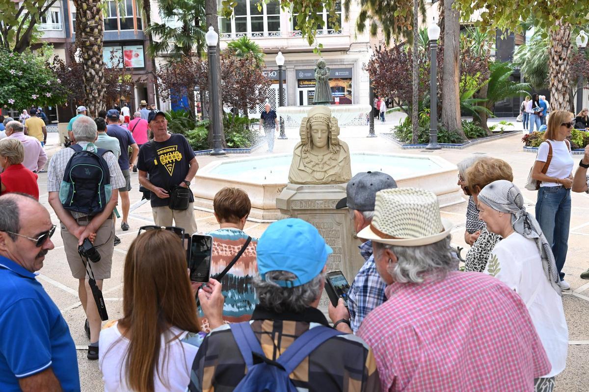Un guía explica a los turistas en la Glorieta la historia del hallazgo de la Dama de Elche frente a una réplica