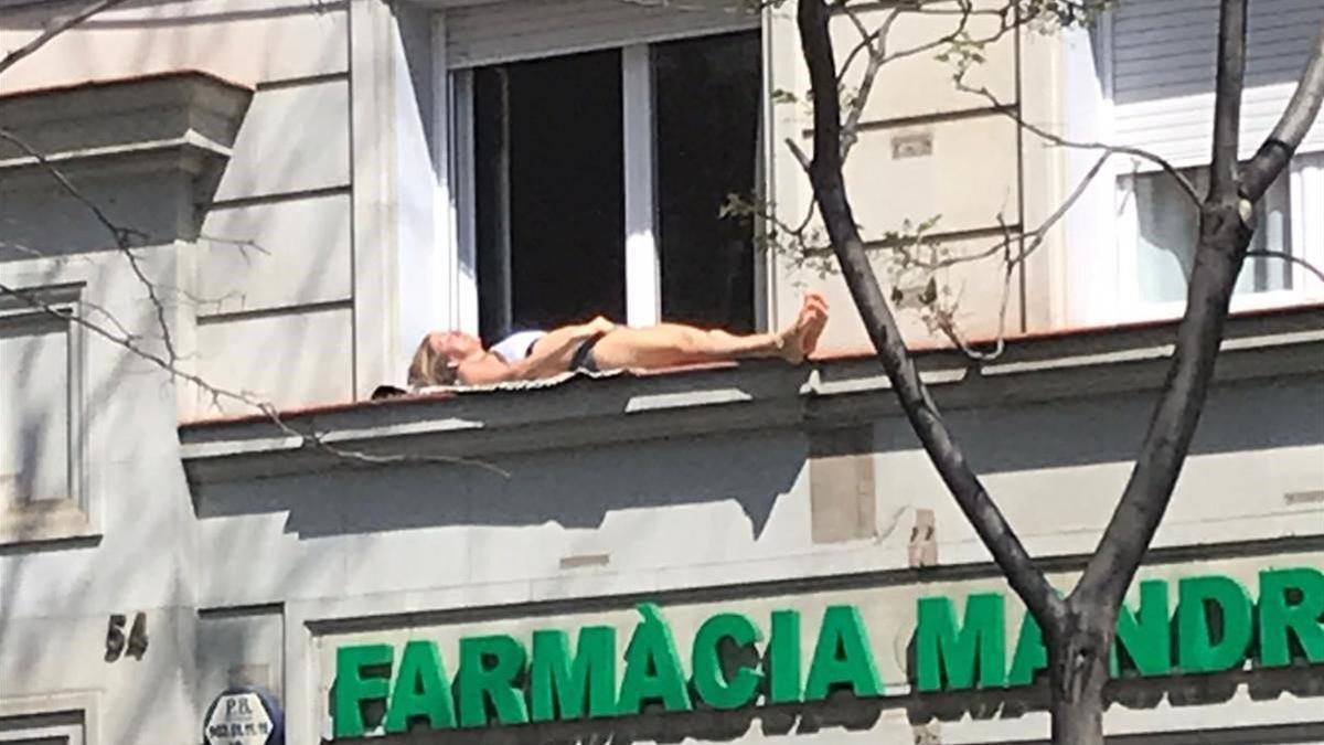 Una mujer toma el sol en la cornisa de una ventana en la calle de Mandri.