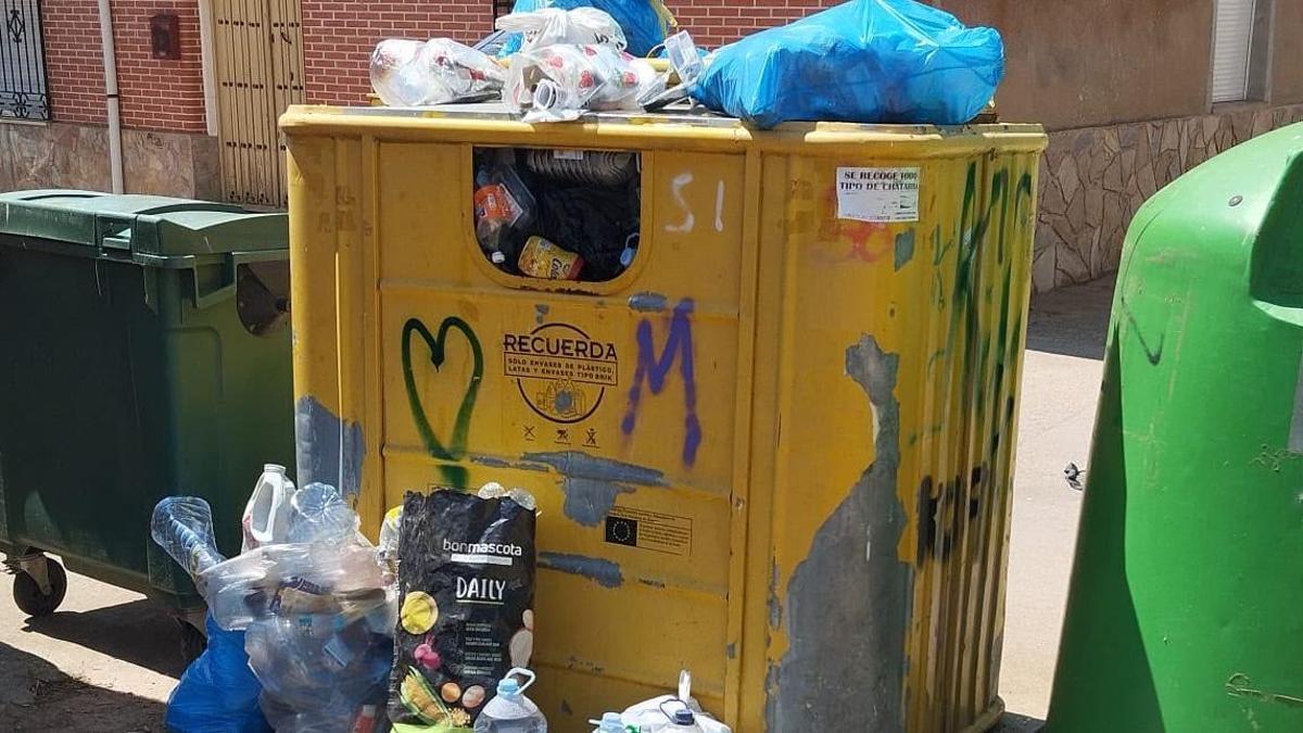 Bolsas de residuos sobre el contenedor y envases en el suelo junto a los contenedores.