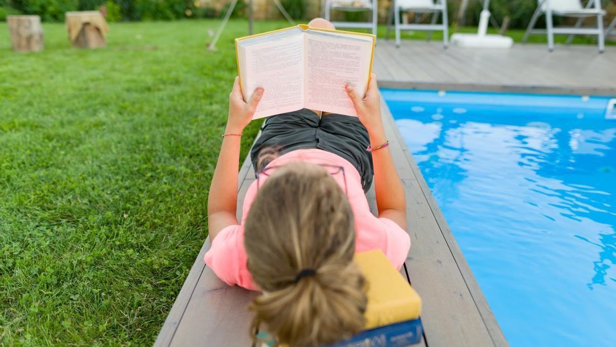 Una adolescente, leyendo un libro en la piscina.