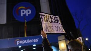 Un hombre sostiene un cartel contra el líder de los populares, Pablo Casado, y en defensa de la presidenta de la Comunidad de Madrid, Isabel Díaz Ayuso, frente a la sede del PP en la madrileña calle de Génova, este 18 de febrero de 2022.