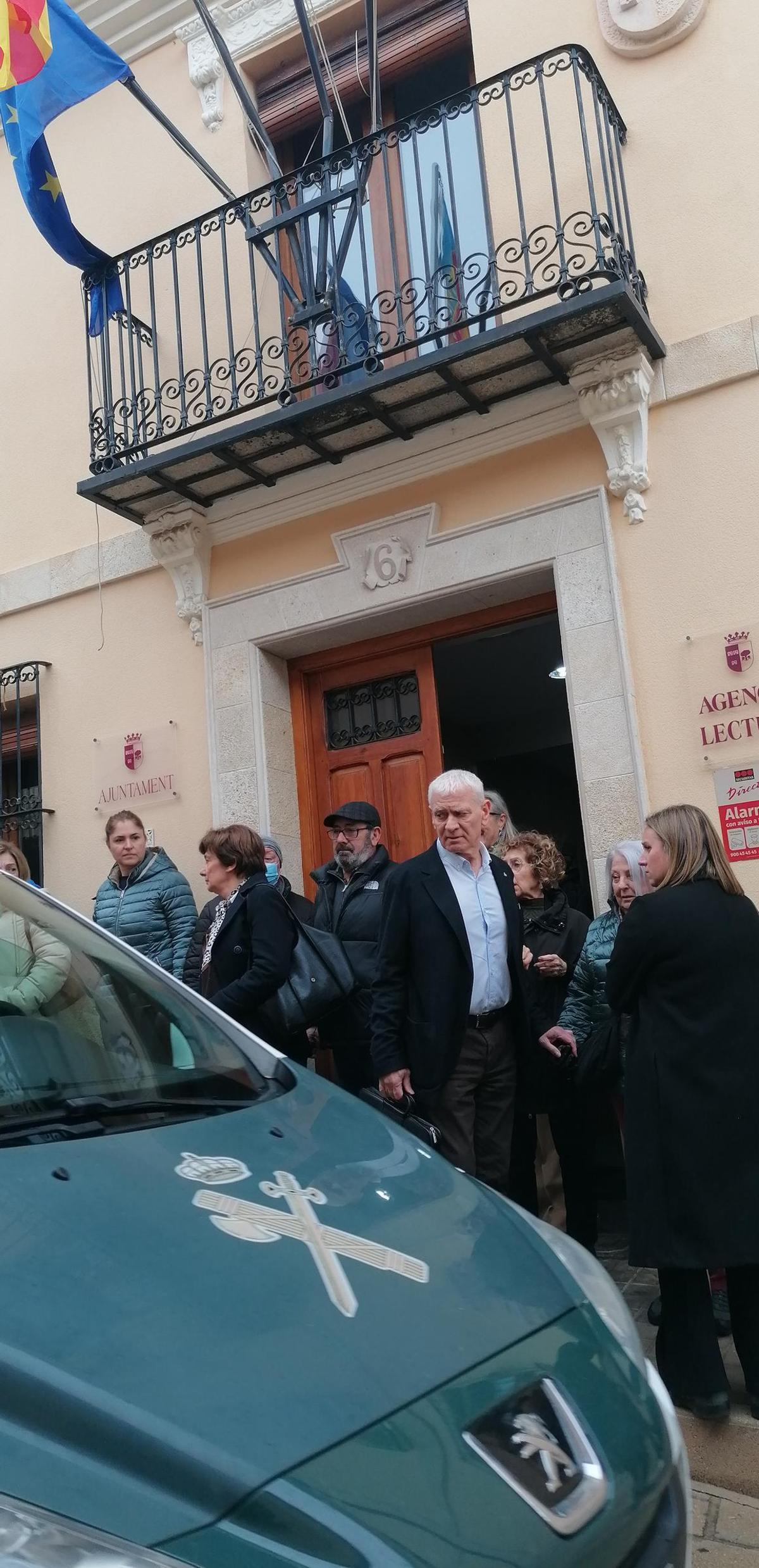 Un vehículo de la Guardia Civil pasa frente al Ayuntamiento de l'Alqueria d'Asnar este viernes, con vecinos que se han acercado para ver qué pasa con el Ayuntamiento