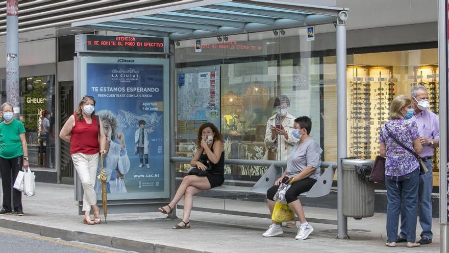 Varias personas con mascarilla en una parada de autobús del centro de Alicante.