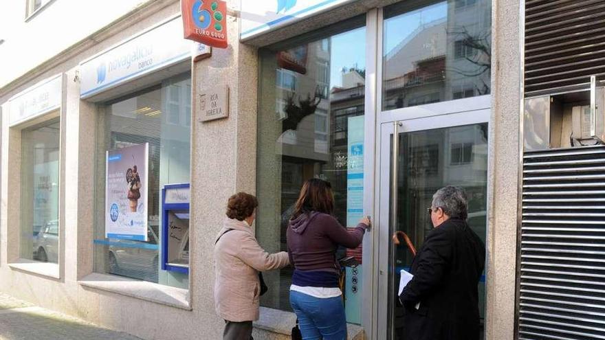 Tres clientes ante una oficina de Novagalicia Banco.