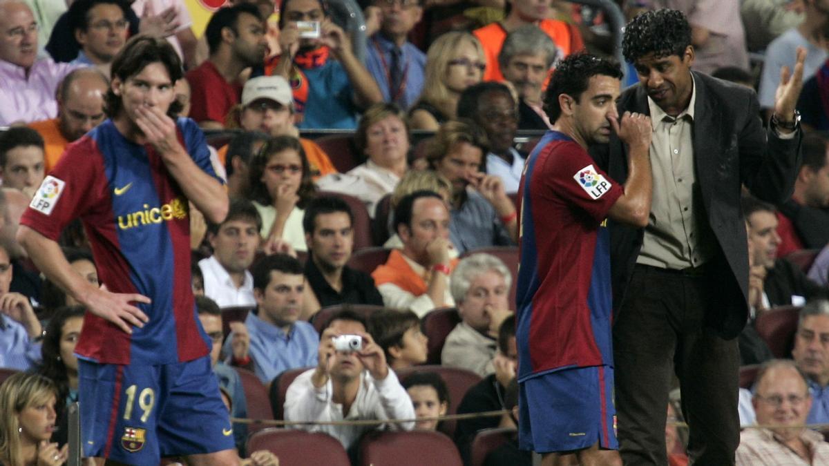 Messi espera mientras Rijkaard habla con Xavi en un partido ante el Valencia en el Camp Nou.