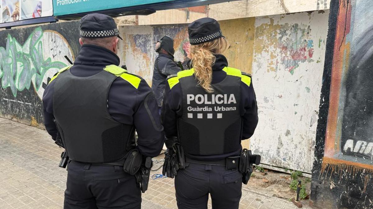 Una pareja de la Guardia Urbana de Badalona presencia como un operario sella la entrada del solar, recientemente desocupado