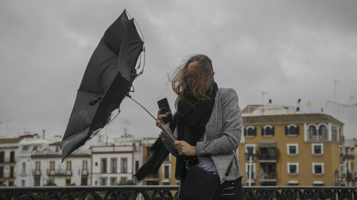 Una racha de viento desbarata el paragüas de una viandante mientras camina por el Puente de Isabel II.