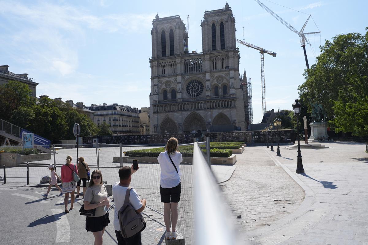 People take photographs of Notre Dame cathedral from outside the security zone set up for the Olympic Games, Thursday, July 18, 2024 in Paris. Starting Thursday, parts of the French capital will only be accessible to people who have registered for a QR code, as part of the massive security operation ahead of the Paris 2024 Olympic Games. (AP Photo/David Goldman)