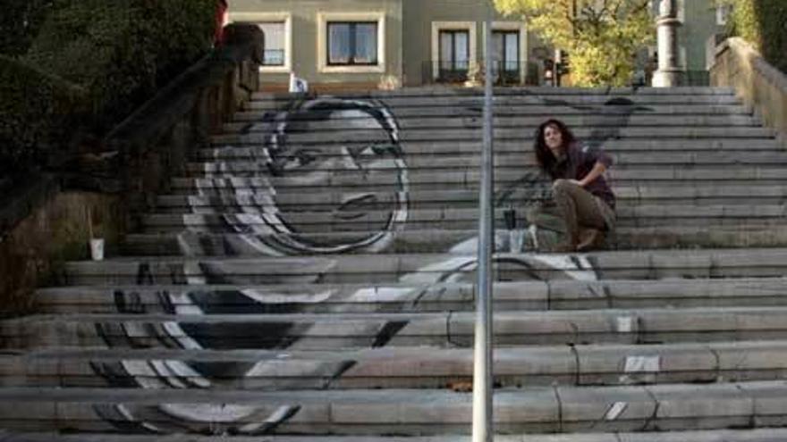 Belen Deniz sentada en las escaleras del Campillín junto al mural que pinta.