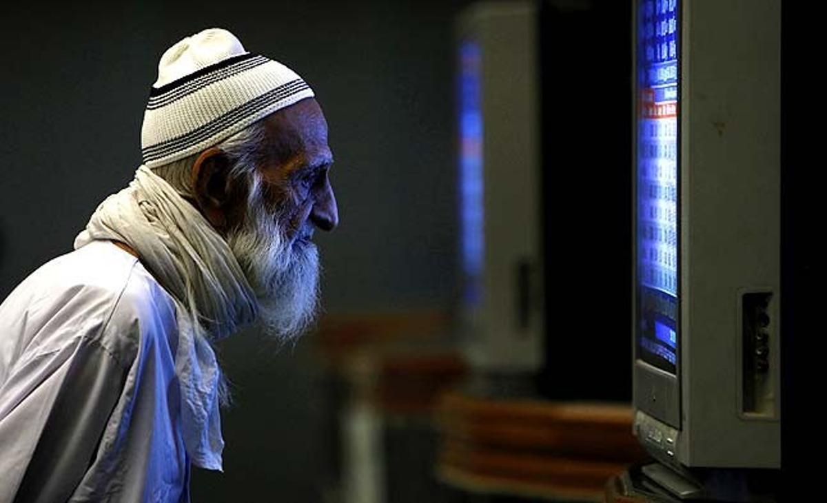 Un home observa el preu de les accions en una pantalla de televisió durant una sessió de negociació a la Borsa de Karachi (Pakistan).