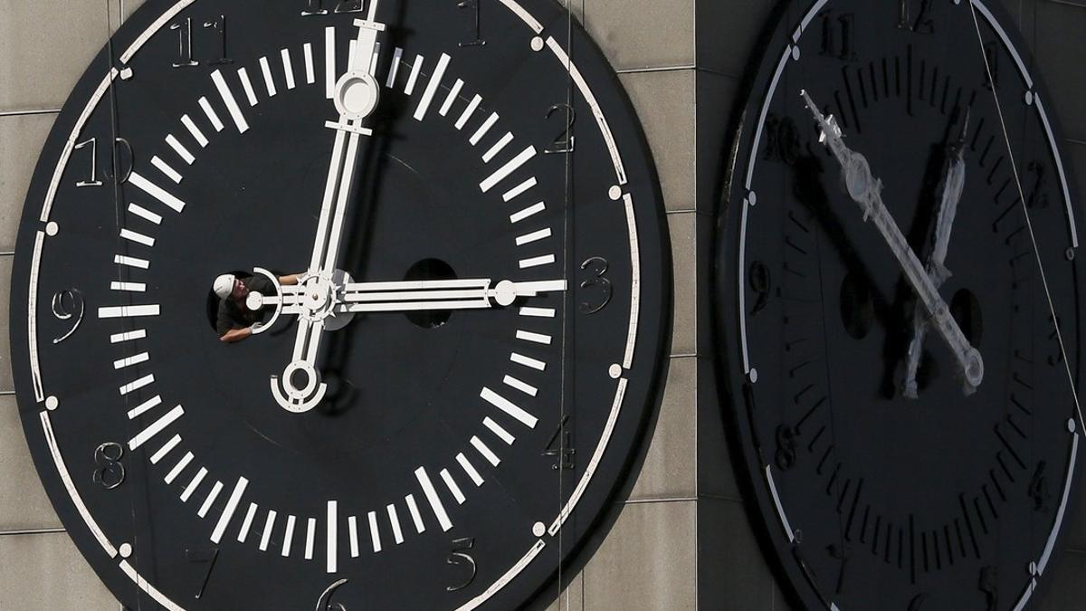 Worker adjusts hands on clock face of city administration building during clock's restoration in Krasnoyarsk