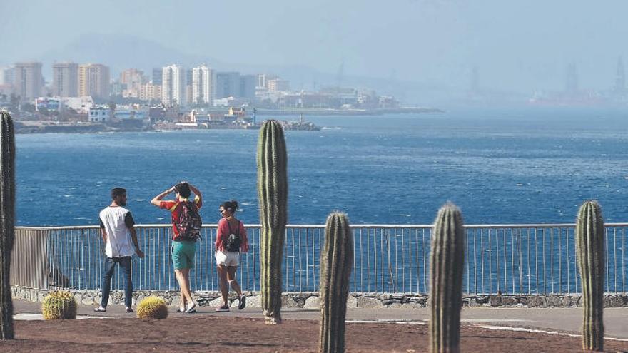 Tres personas pasean en la zona de La Laja, con un horizonte difuminado por la calima