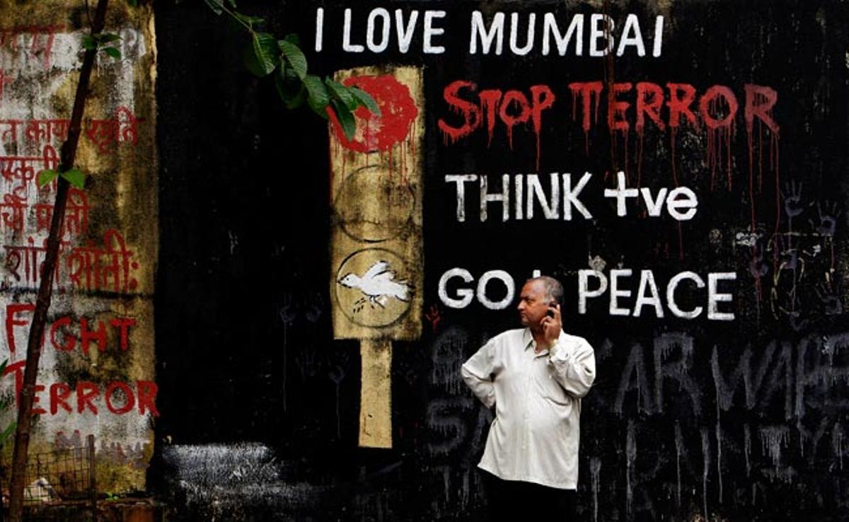 Un home conversa davant les pintades que rememoren els atacs terroristes que s’han produït el 2008 contra hindús a Mumbai, a l’Índia.