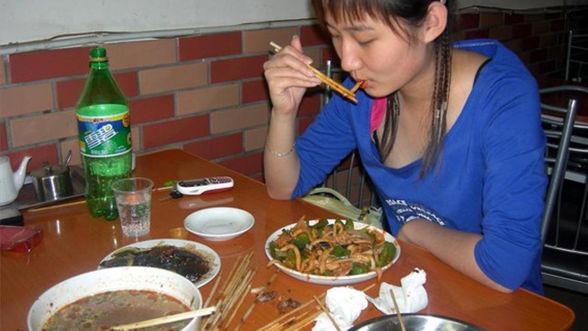 Una joven come con palillos en un restaurante de Pekín.