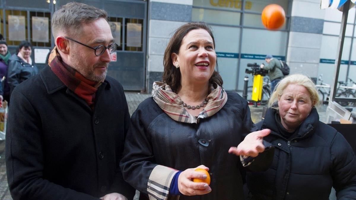 Mary Lou McDonald lanza una naranja al aire durante una visita a un puesto de fruta callejero en Dublín, este lunes.
