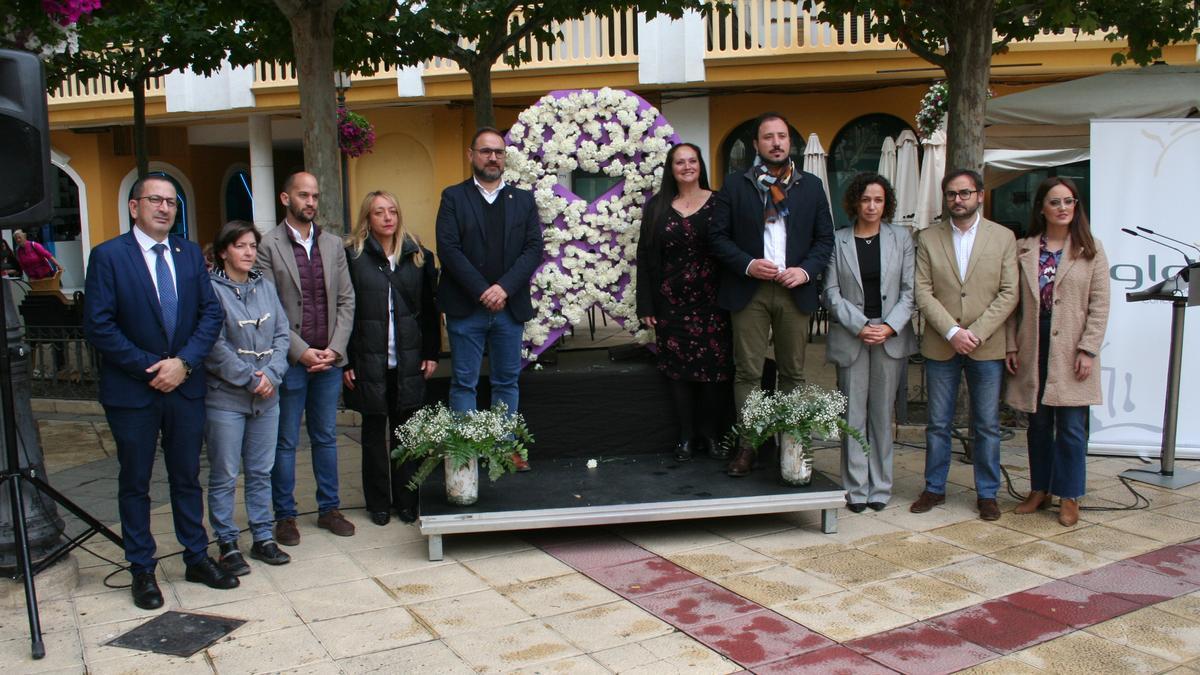 José Luis Ruiz, María Dolores Chumilla, José Ángel Ponce, María Ángeles Mazuecos, Diego José Mateos, Antonia Pérez, Francisco Morales, Isidro Abellán e Irene Jódar ante el lazo violeta cubierto de claveles blancos en señal de recuerdo por cada una de las víctimas de la violencia machista.