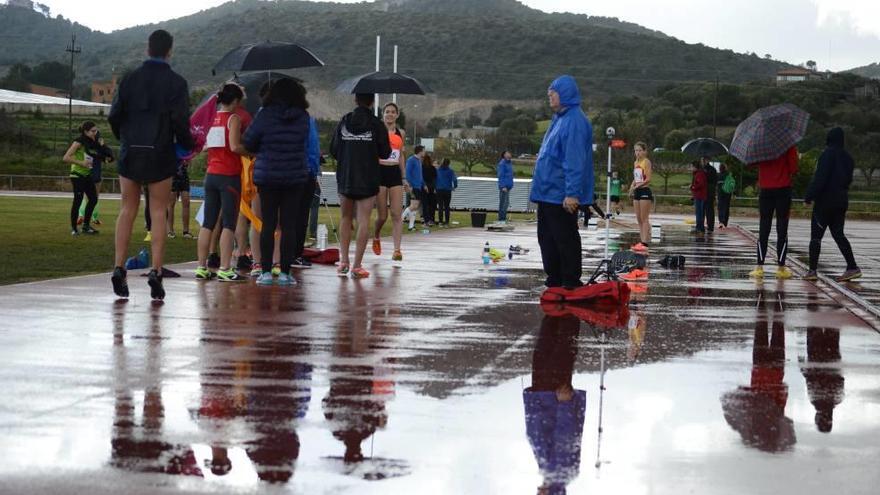 Atletas y técnicos, con paraguas, sobre los charcos del tartán que acogió en Manacor el Campeonato de Balears de pista cubierta.