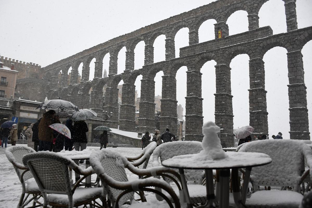 Varias personas caminan junto al Acueducto de Segovia que este sábado se ha cubierto por la nieve.