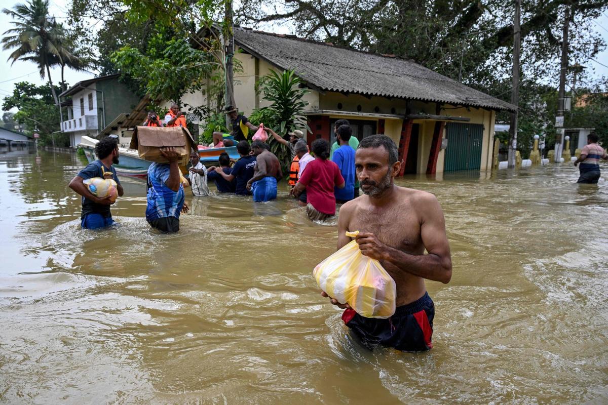 Residents carrying belongings wade through a flooded area after heavy rainfall in Wellampitiya on the outskirts of Colombo on December 1, 2025. At least 340 people have been killed, Sri Lankan officials said on December 1, with many more still missing. (Photo by Ishara S. KODIKARA / AFP)