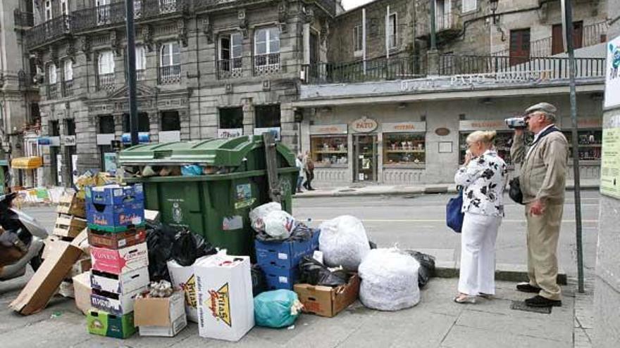 Dos turistas filman la céntrica Puerta del Sol donde los contenedores de basura rebosaban de desperdicios.