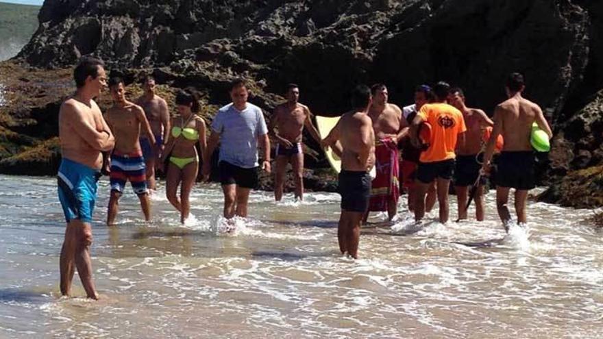 Uno de los bañistas rescatados en Sorraos, con la toalla, junto a otros usuarios y los socoristas.