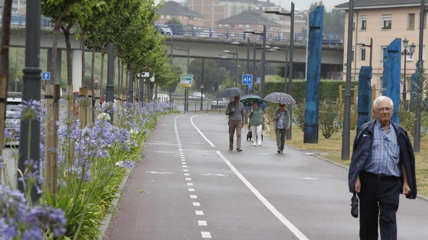 Viandantes paseando ayer por el parque lineal a pesar de la lluvia. | FERNANDO RODRÍGUEZ