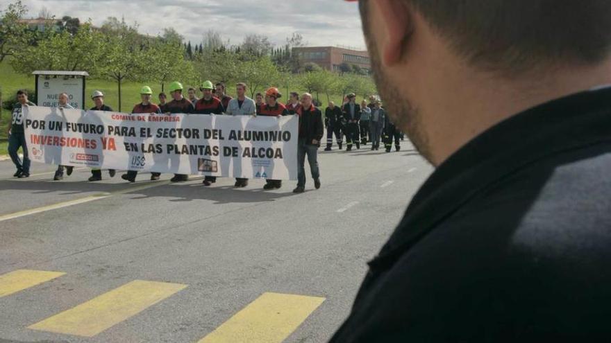 Un trabajador de Alcoa, de espaldas, mira el avance de un grupo de compañeros que portan una pancarta reivindicando la realización de inversiones en las fábricas de la multinacional.