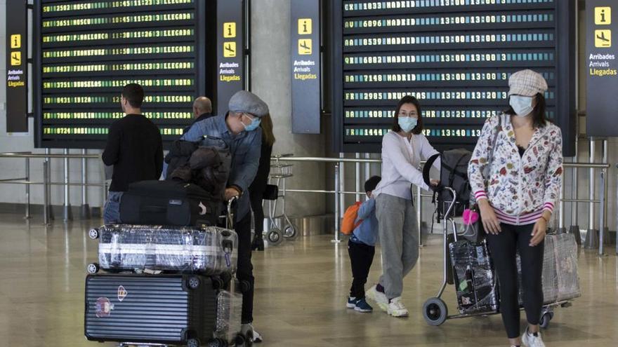 Varios pasajeros con mascarilla buscan su puerta de embarque en un aeropuerto.