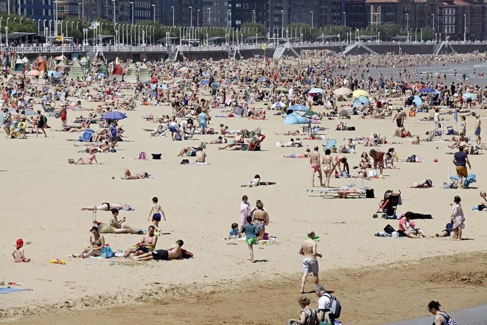 Gijoneses y visitantes se lanzan a la playa en una jornada calurosa.