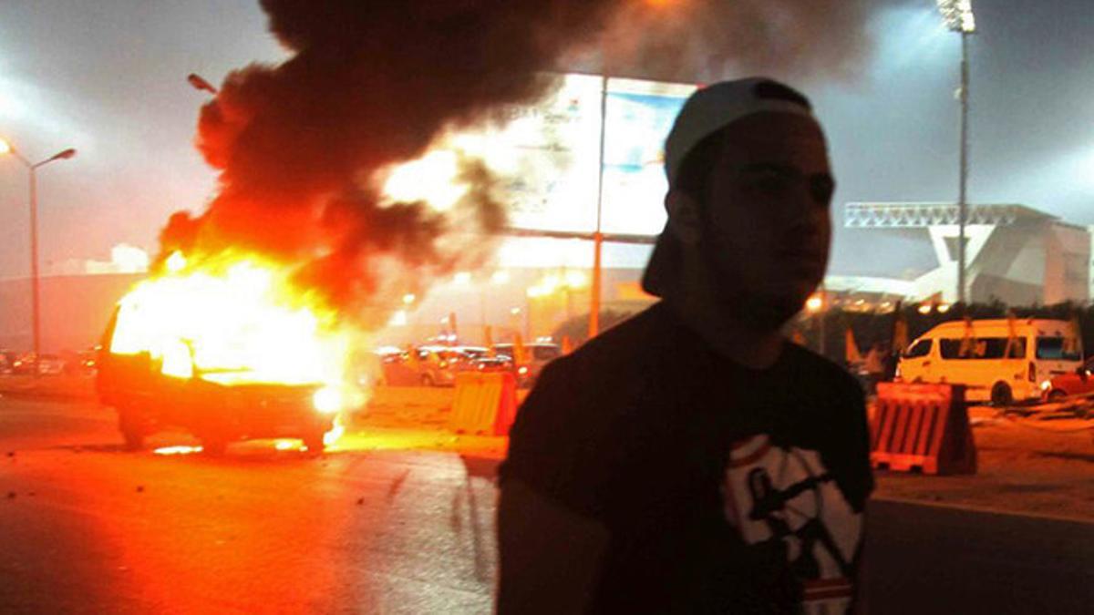 Un aficionado al fútbol pasa junto a un coche en llamas, durante los enfremtamientos entre ultras y policías en El Cairo
