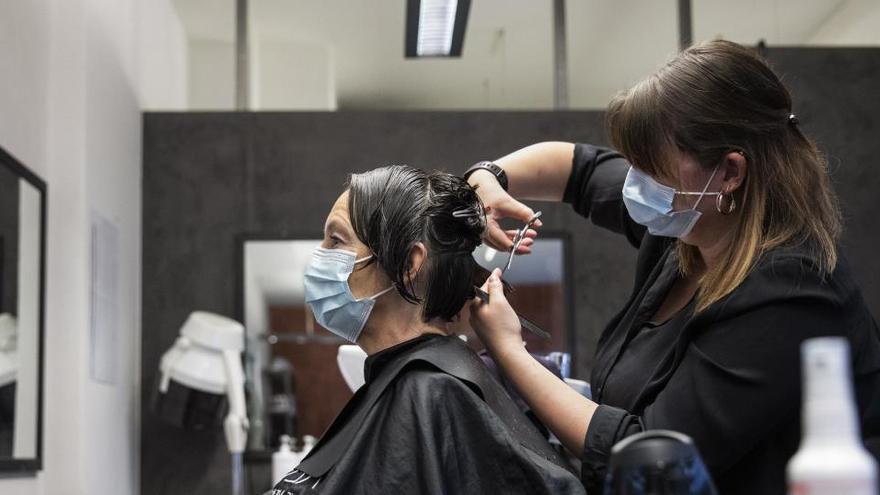 Una peluquera corta el pelo a una mujer con mascarilla en Berna.