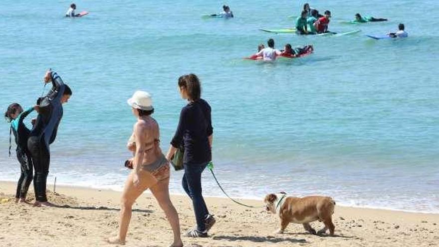 Dos mujeres pasean por la orilla, entre los surfistas. // Diputación