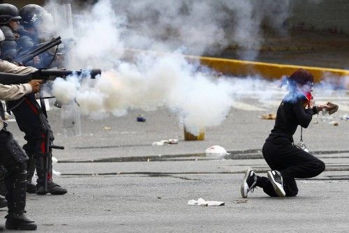 Venezuela's national police fire tear gas as an anti-government protester kneels holding a rock during riots in Caracas