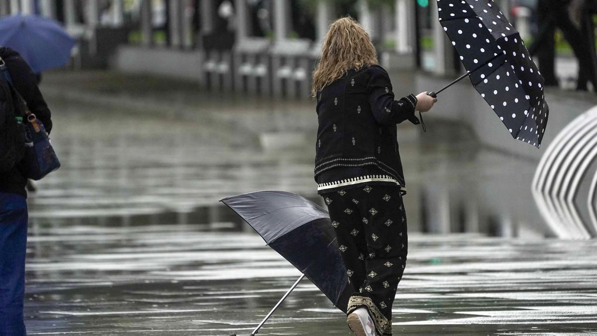 Una mujer se intenta proteger de la lluvia y el viento con un paraguas.