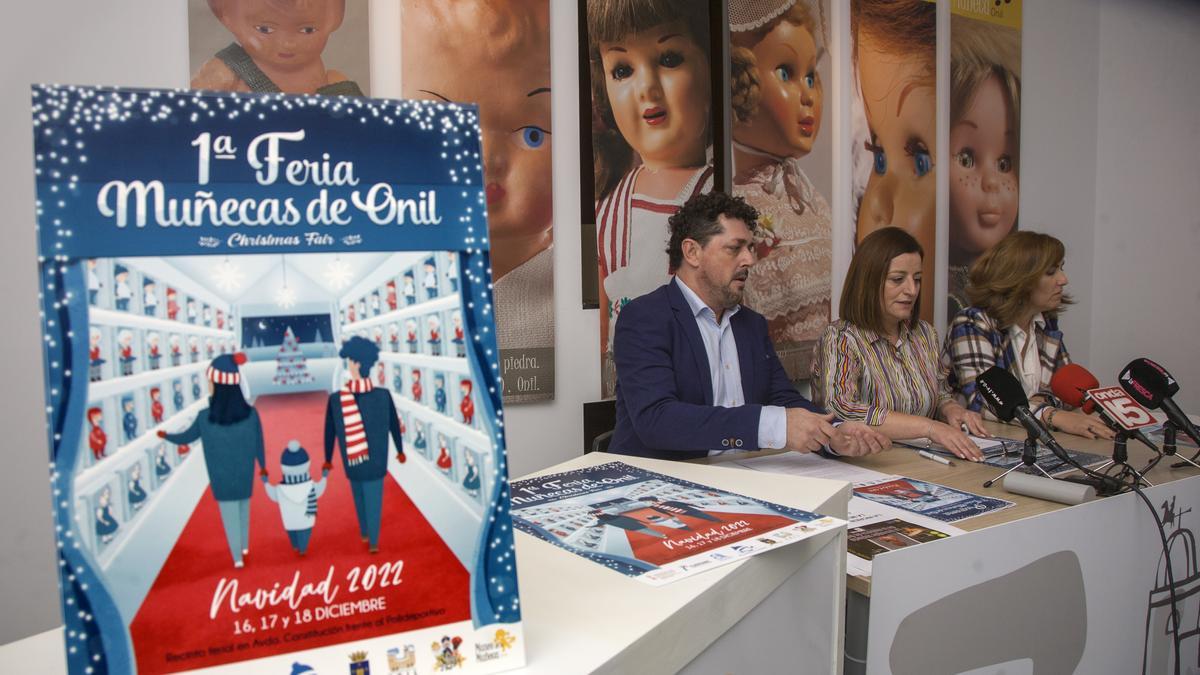 Cartel de la Feria de Muñecas de Onil durante la presentación del certamen, con la alcaldesa entre los ediles de Turismo y Comercio.