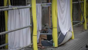 Personas duermen en la calle sobre colchones junto a comercios de la zona de Trafalgar-Méndez Núñez, a primera hora de la mañana. Comerciantes y vecinos denuncian la degradación del entorno y los continuos cortes de luz que afectan al barrio. A media mañana, la zona recupera su actividad habitual, con turistas y vecinos en las calles, tiendas y restaurantes abiertos y locales con carteles de «Se alquila», mientras en las aceras todavía pueden verse agujeros y obras de reparaciones recientes. Barcelona, 10 de agosto de 2026. Sociedad. AUTOR: MANU MITRU.