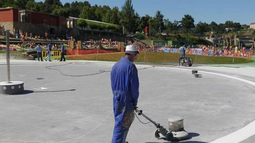 Un operario pule la piscina infantil mientras, al fondo, decneas de personas usan la de adultos.